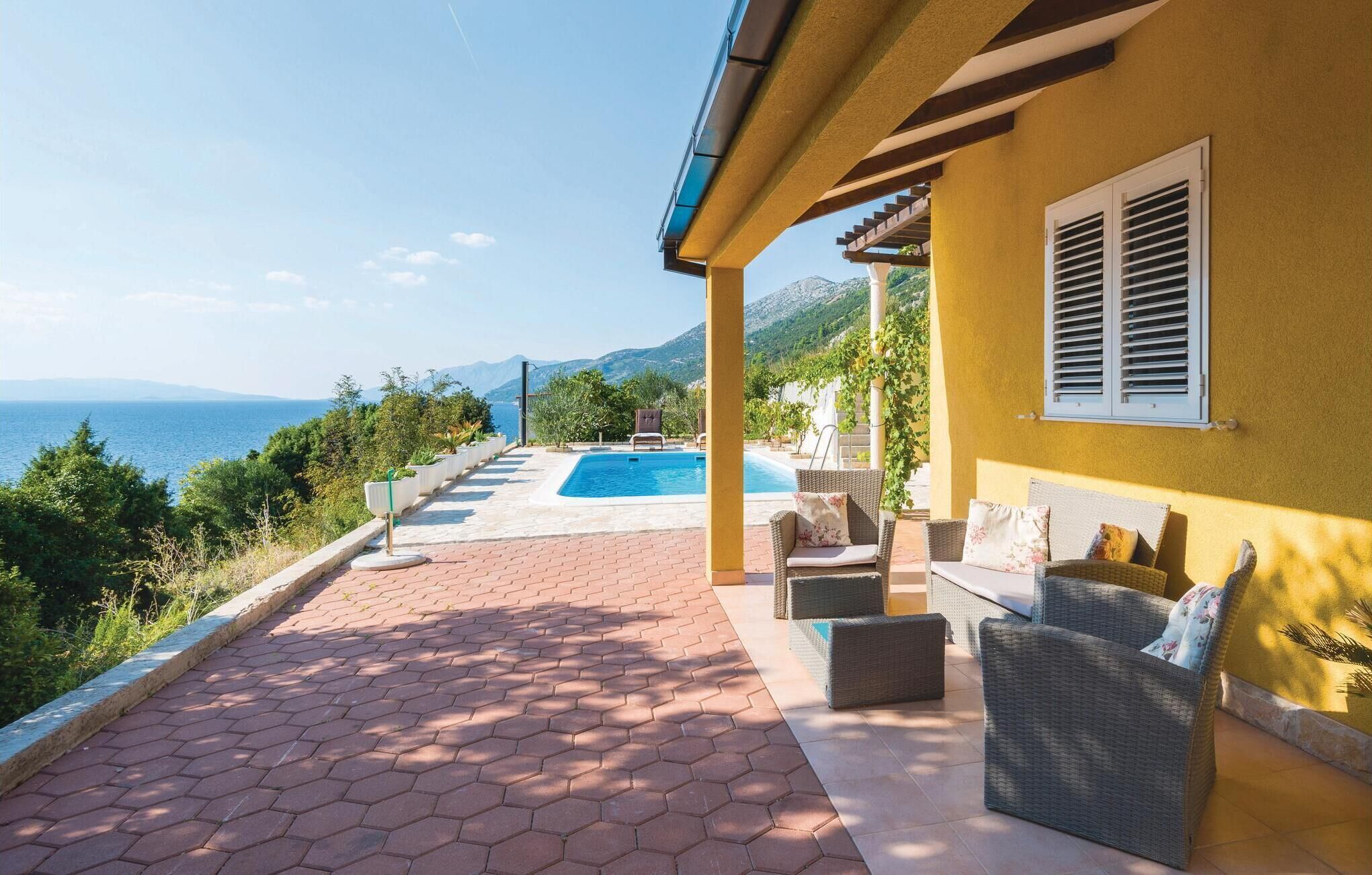 A pool area with a view of the sea, outdoor furniture, and a yellow building.