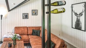 Ein Wohnzimmer mit braunem Sofa, einem Couchtisch, einem an der Wand befestigten Weinkühlschrank mit Flaschen, gerahmten Kunstwerken und einem großen Hirschbild.