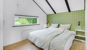 Ein Schlafzimmer mit Bett, Fenster, Nachttisch und grüner Wand.
