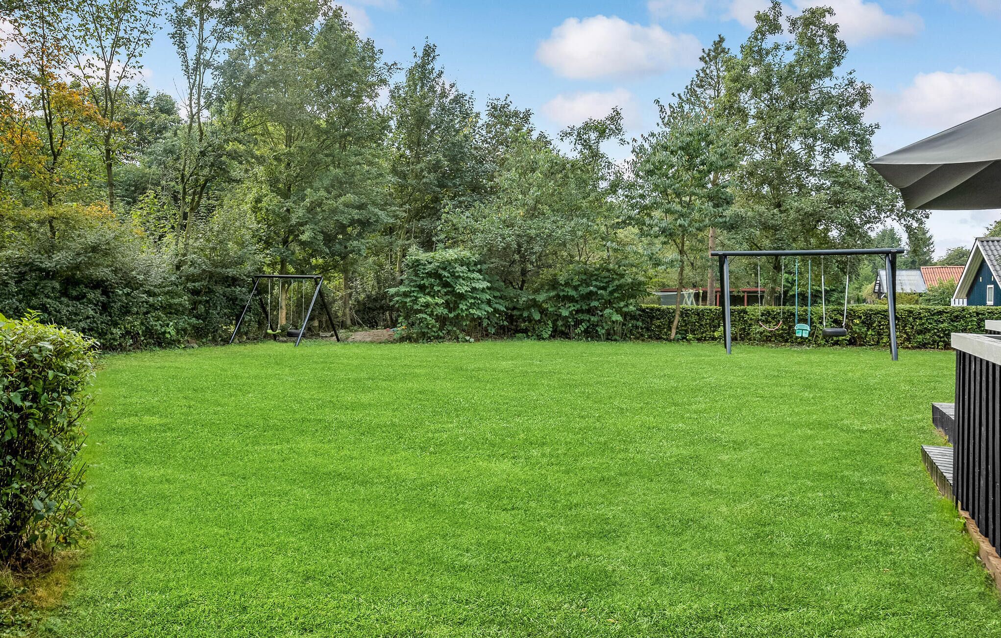 Un jardin bien entretenu avec une pelouse verdoyante, une balançoire et une clôture en bois.