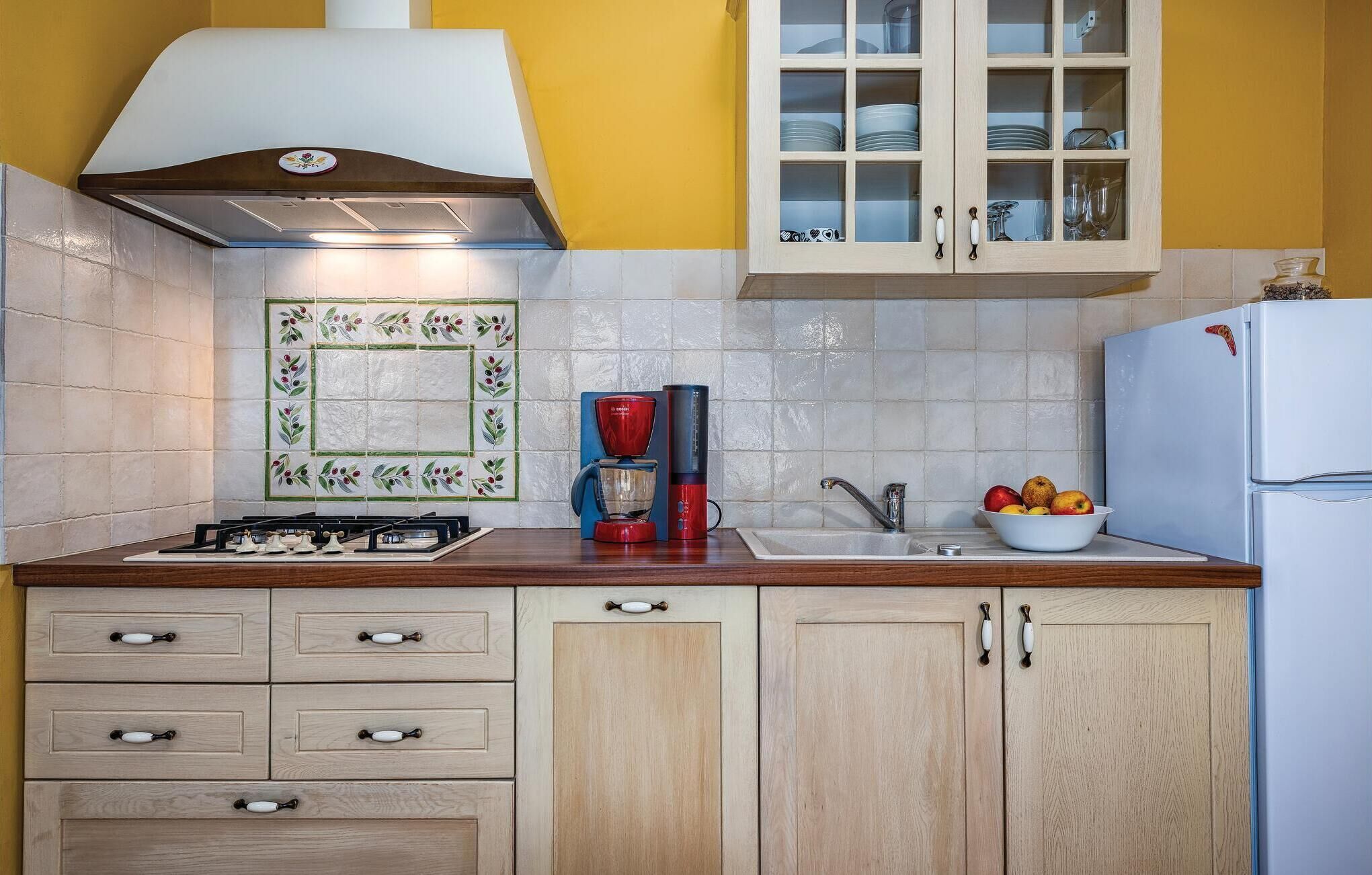 A kitchen with a gas stove, a coffee maker, a sink, and a bowl of fruit.