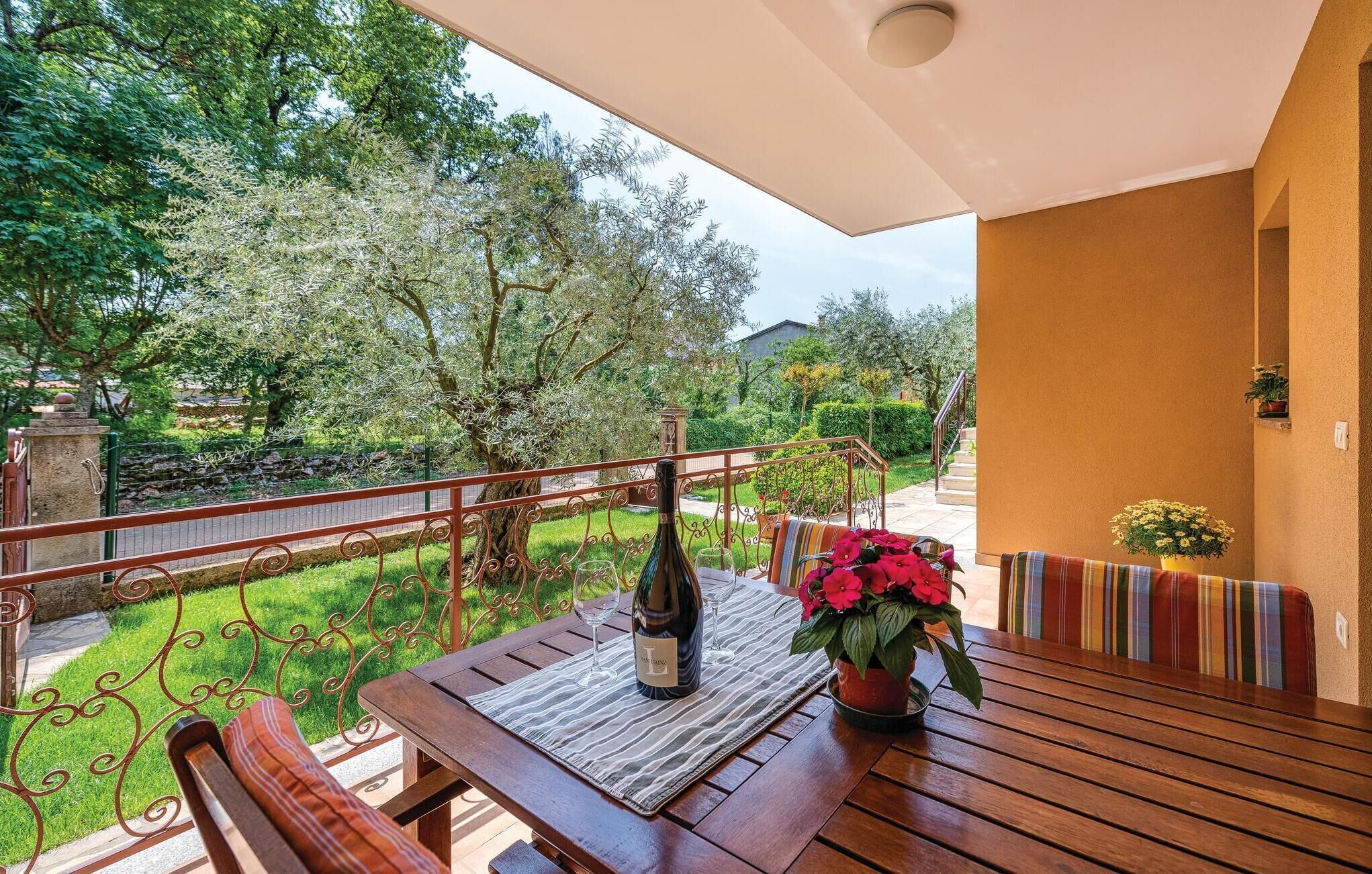 En udendørs terrasse med et træbord, en vinflaske og en potteplante.
