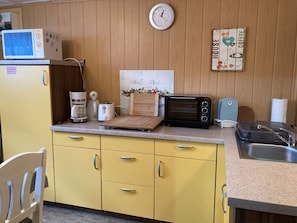A compact kitchen with a microwave, toaster, coffee maker, and a wooden cutting board.