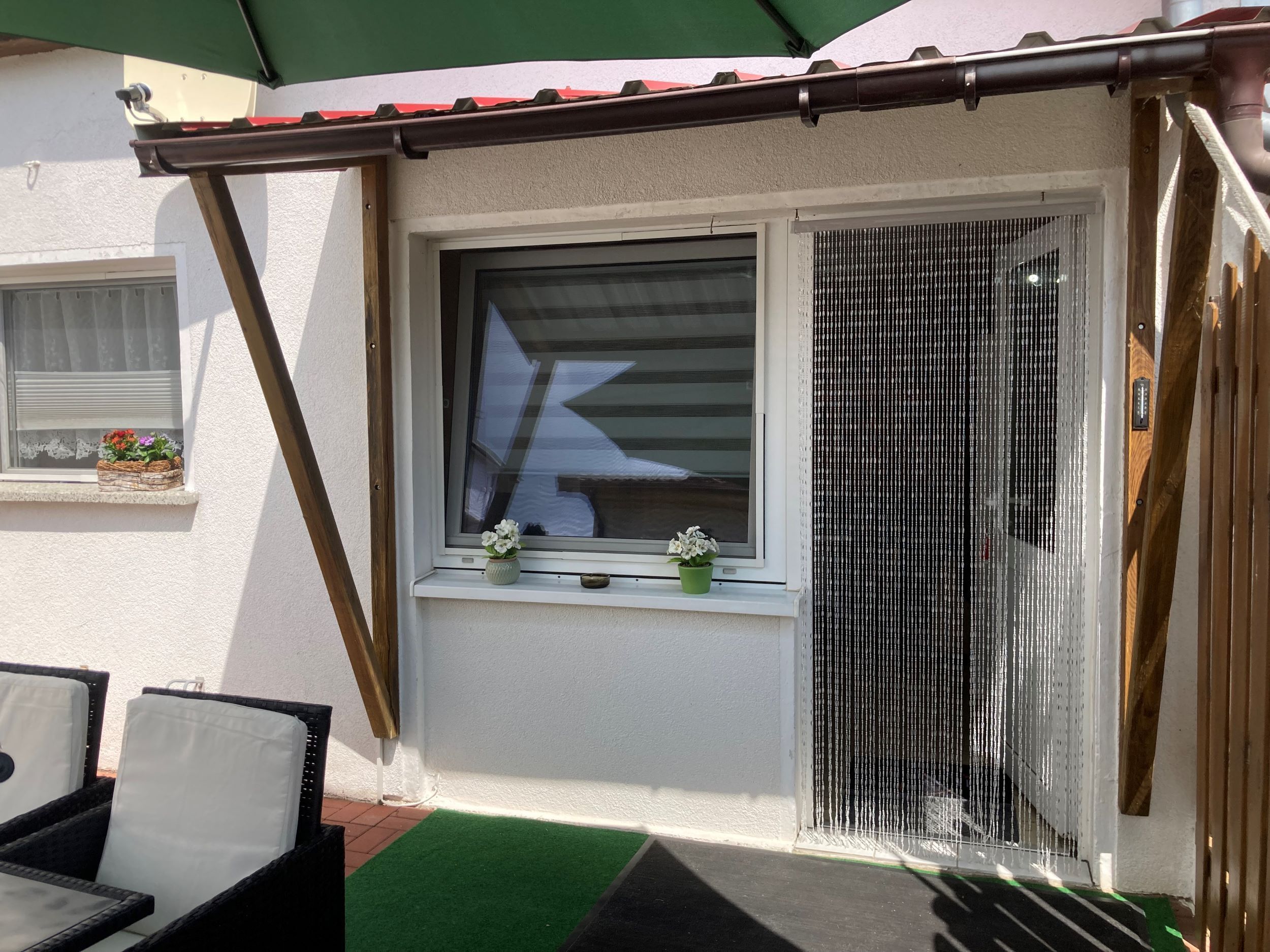 A patio area with a window, a green awning, and a small table with chairs.