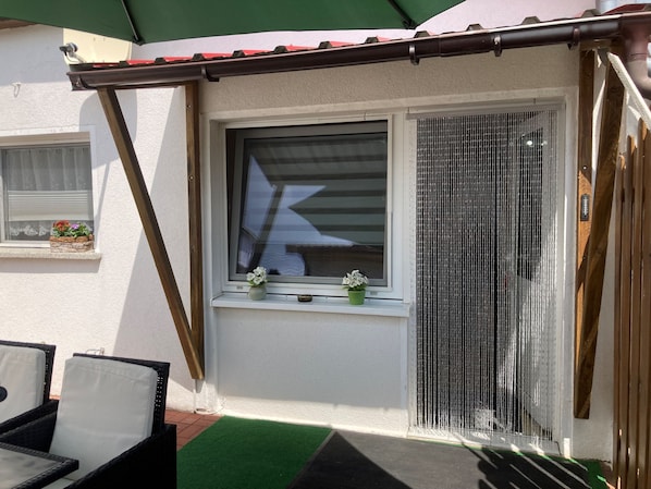 A patio area with a window, a green awning, and a small table with chairs.