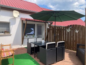A patio with a table and chairs, a green umbrella, and a wooden fence.