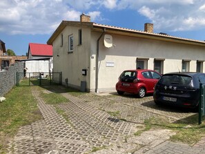 A building with a paved driveway, a red car, and a black car parked in front.
