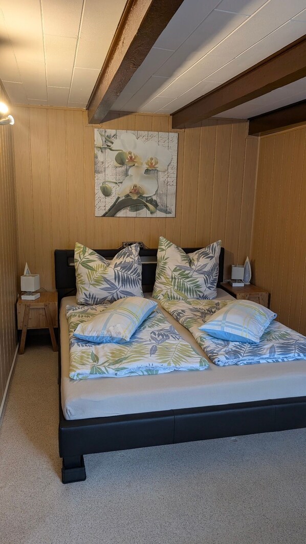 A bedroom with a wooden paneled wall, a bed with floral bedding, and a painting of orchids.