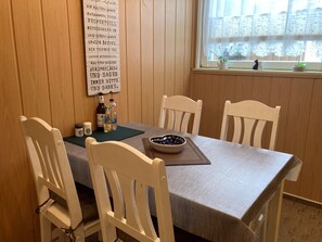A dining area with a wooden table, four white chairs, a placemat, a bowl, and a bottle of water.