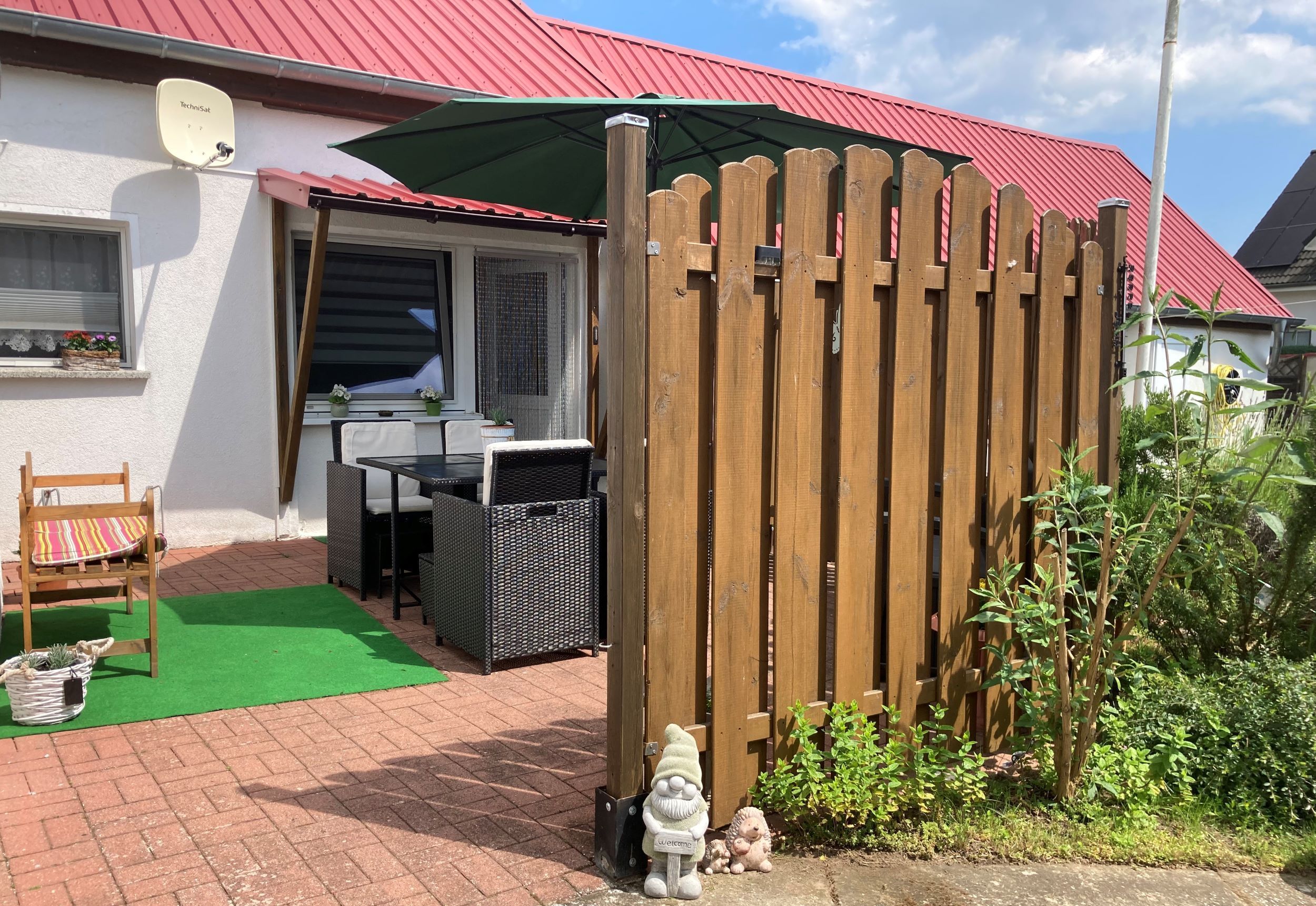 A wooden fence, a garden gnome, and a patio area with a table and chairs.
