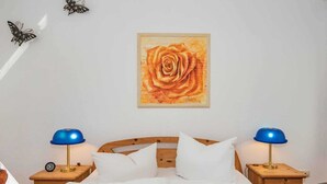 A hotel room with a wooden bed, two blue lamps, a clock, and a framed painting of a rose on the wall.