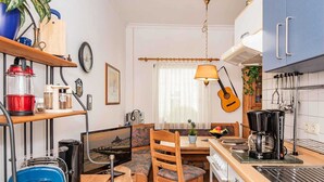 A compact kitchen with a dining area, wooden furniture, and a guitar hanging on the wall.