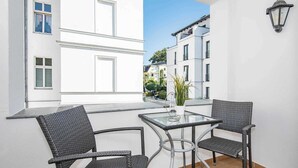 A balcony with two wicker chairs, a glass table, and a potted plant.