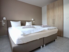 A modern hotel room with a large bed, two bedside tables, a wardrobe, and a wall-mounted lamp.