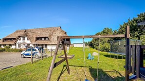 A house with a thatched roof, a swing set, and a trampoline in the yard.