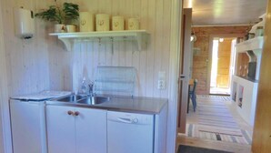 Cozinha compacta com armários brancos, lava-louças, pia e uma planta pendurada.