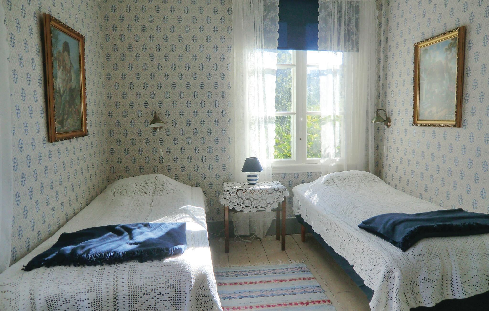 A room with two single beds, a small table with a lamp, and a window with curtains.
