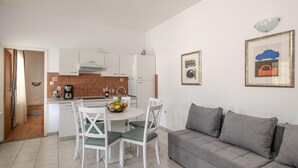 Una cocina moderna con armarios blancos, una mesa de comedor con sillas y un sofá gris.