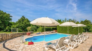 Una piscina con sillas de descanso y sombrillas, rodeada de baldosas de piedra y follaje.