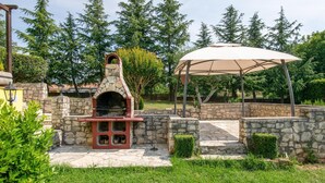 Un área de barbacoa de piedra al aire libre con chimenea, un espacio cubierto para sentarse y un muro de piedra que rodea el área.