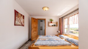 A bedroom with a wooden bed, a door leading to a bathroom, a shelf with plants, and a window with curtains. - Apartment garden view - 2-room apartment garden view (Rerik)