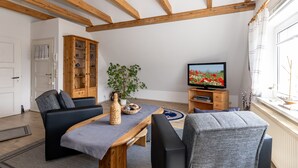 A living room with wooden beams, a television, a sofa, a coffee table, and a cabinet. - Apartment garden view - 2-room apartment garden view (Rerik)