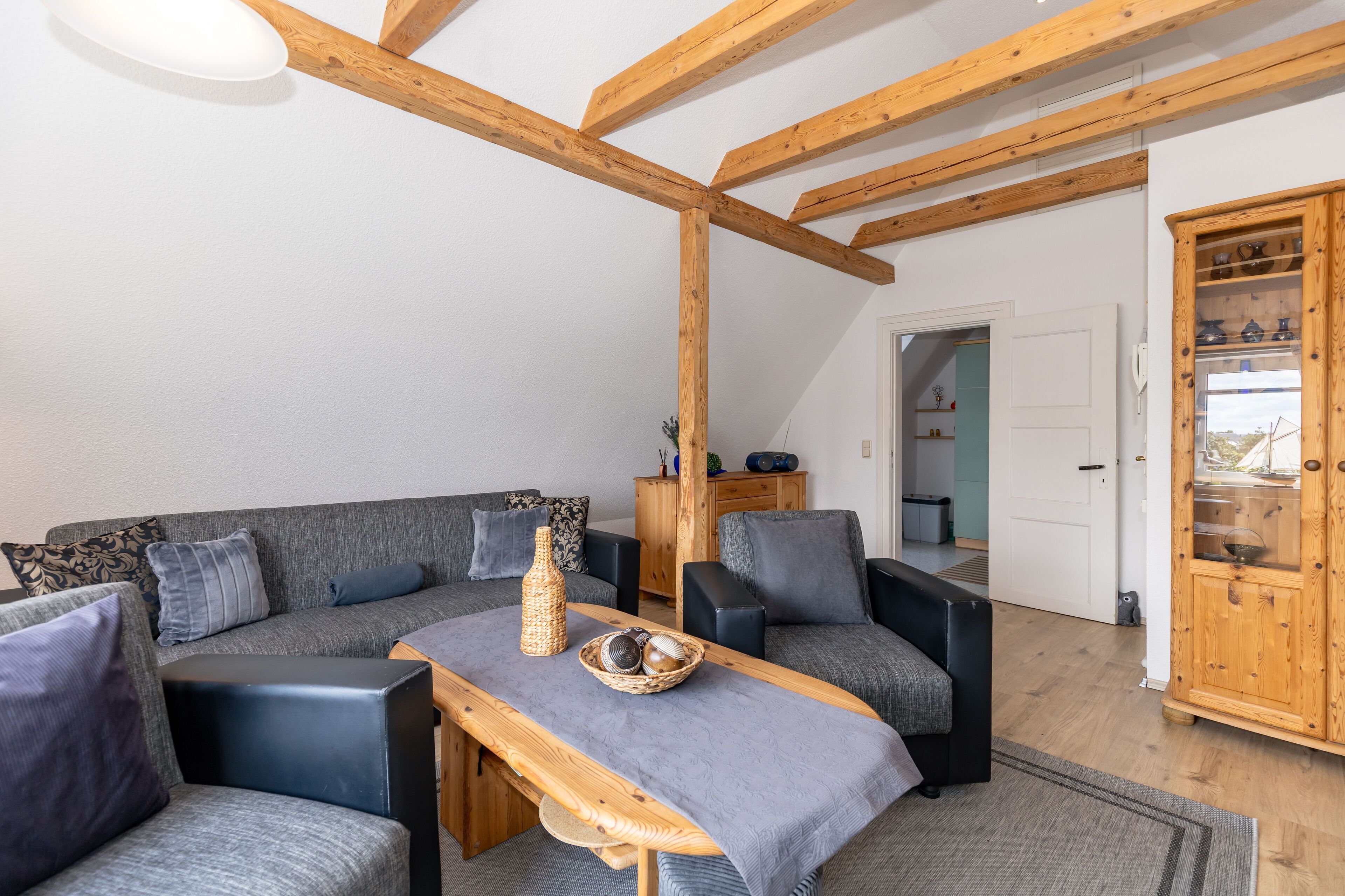 Ein modernes Wohnzimmer mit Holzboden, grauen Sofas, einem Holztisch und einer Vitrine.