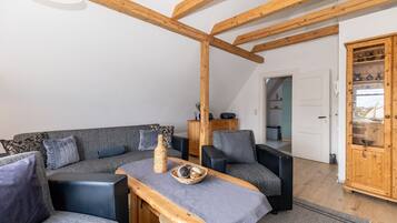 Ein modernes Wohnzimmer mit Holzboden, grauen Sofas, einem Holztisch und einer Vitrine.