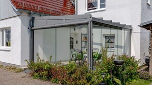 A modern house with a glass-enclosed patio area featuring outdoor furniture. - Apartment garden view - 2-room apartment garden view (Rerik)