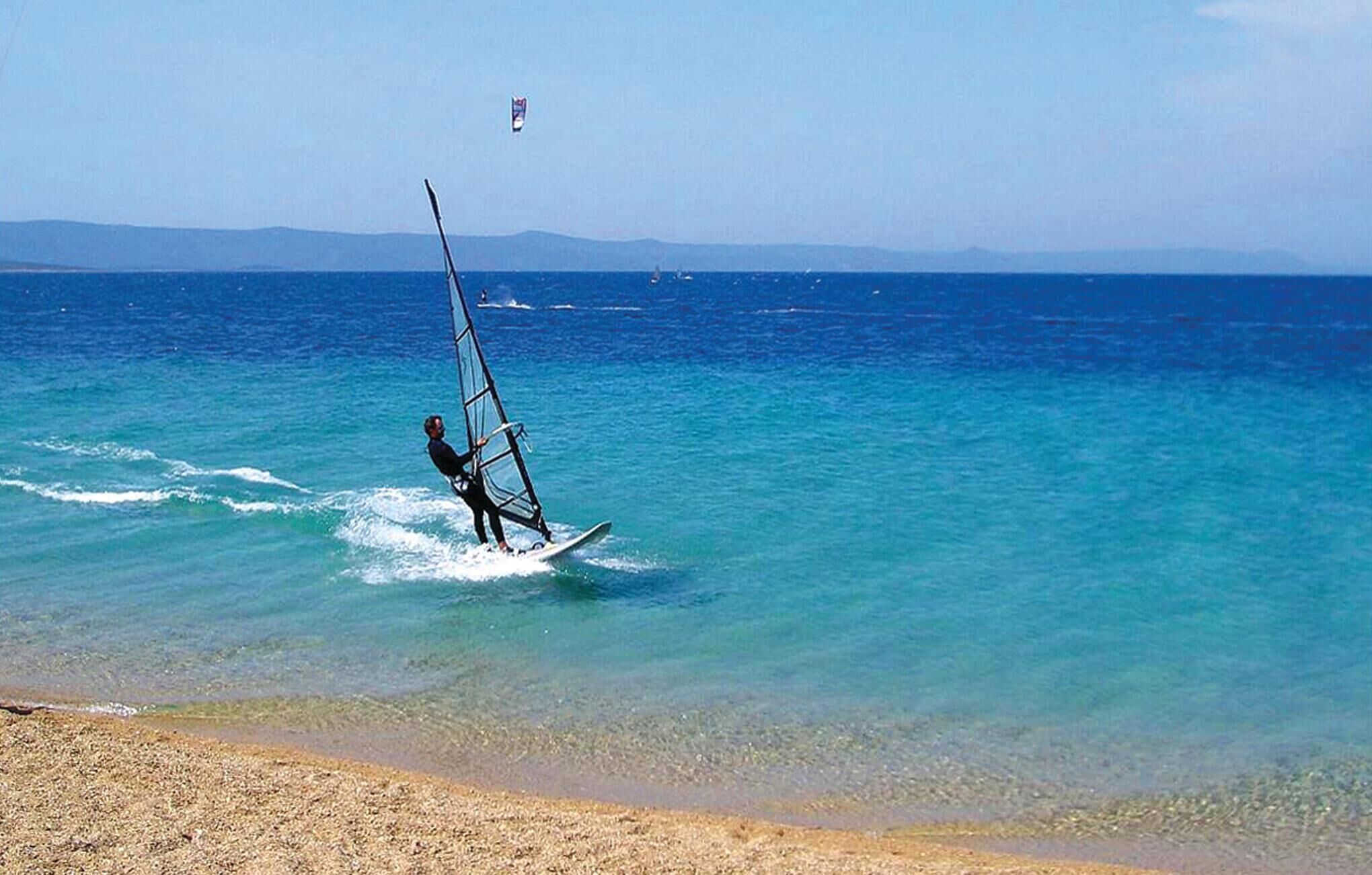 A person windsurfing on a clear day with calm waters and distant mountains.