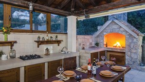 A rustic outdoor kitchen with a stone oven, wooden cabinets, and a dining table set for a meal. - Beach front home in Orebic (Orebic)