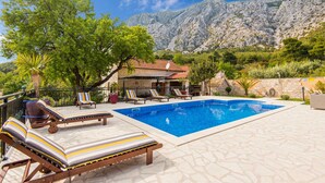 A swimming pool with lounge chairs, a stone building, and a mountainous backdrop. - Beach front home in Orebic (Orebic)