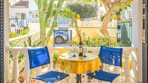 Een balkon met twee blauwe stoelen, een kleine ronde tafel en een fles wijn.