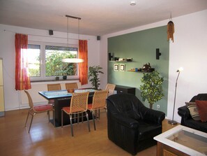 Una sala de estar con comedor, un sofá de cuero negro, una mesa de centro de vidrio y una mesa de comedor con sillas de mimbre.