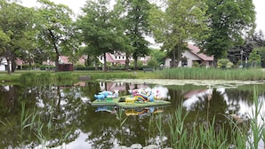 Un étang orné de sculptures d’animaux aux couleurs vives, posées sur une plateforme flottante, entouré d’arbres et avec des maisons en arrière-plan.