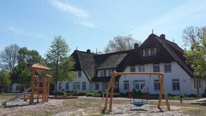 Un terrain de jeux avec un toboggan et des balançoires, une maison au toit de chaume et un ciel dégagé.