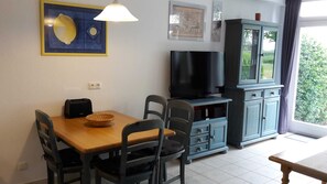 A dining area with a wooden table, four chairs, a basket, a toaster, and a television on a cabinet.