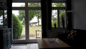 Une pièce dotée d’une grande porte-fenêtre coulissante donnant sur un jardin, d’un canapé, d’une table avec un panier et d’un meuble.