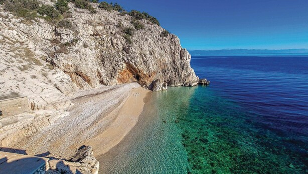 Un paisatge costaner rocos amb aigües blaves cristal·línes i una platja de sorra.