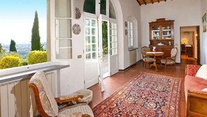 Amplia habitación con un ventanal grande, techo de madera, alfombra estampada, armario de madera y una zona de estar acogedora.