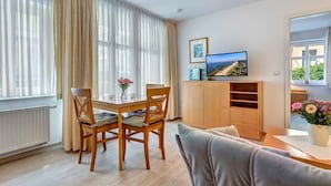 A modern living room with a dining area, a television, and a view of the outdoors. - Villa Aquamarina Whg. 1, SOUTH FACING BALCONY, CHAIR - Villa Aquamarina, 1st ROW, partly. (Heringsdorf)