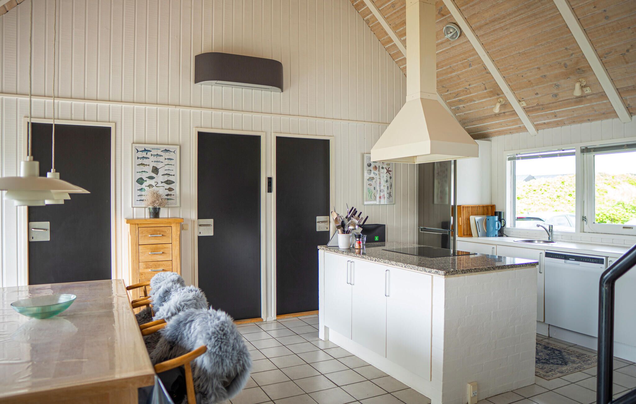 A modern kitchen with white cabinetry, a granite countertop, and a large island. There is a dining area with a wooden table and chairs, and a fluffy dog sitting on the floor.