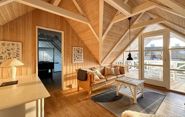 Ein gemütliches Schlafzimmer unter dem Dach mit Holzbalkendecke, einem Sofa, einem kleinen Tisch und Blick ins Freie.