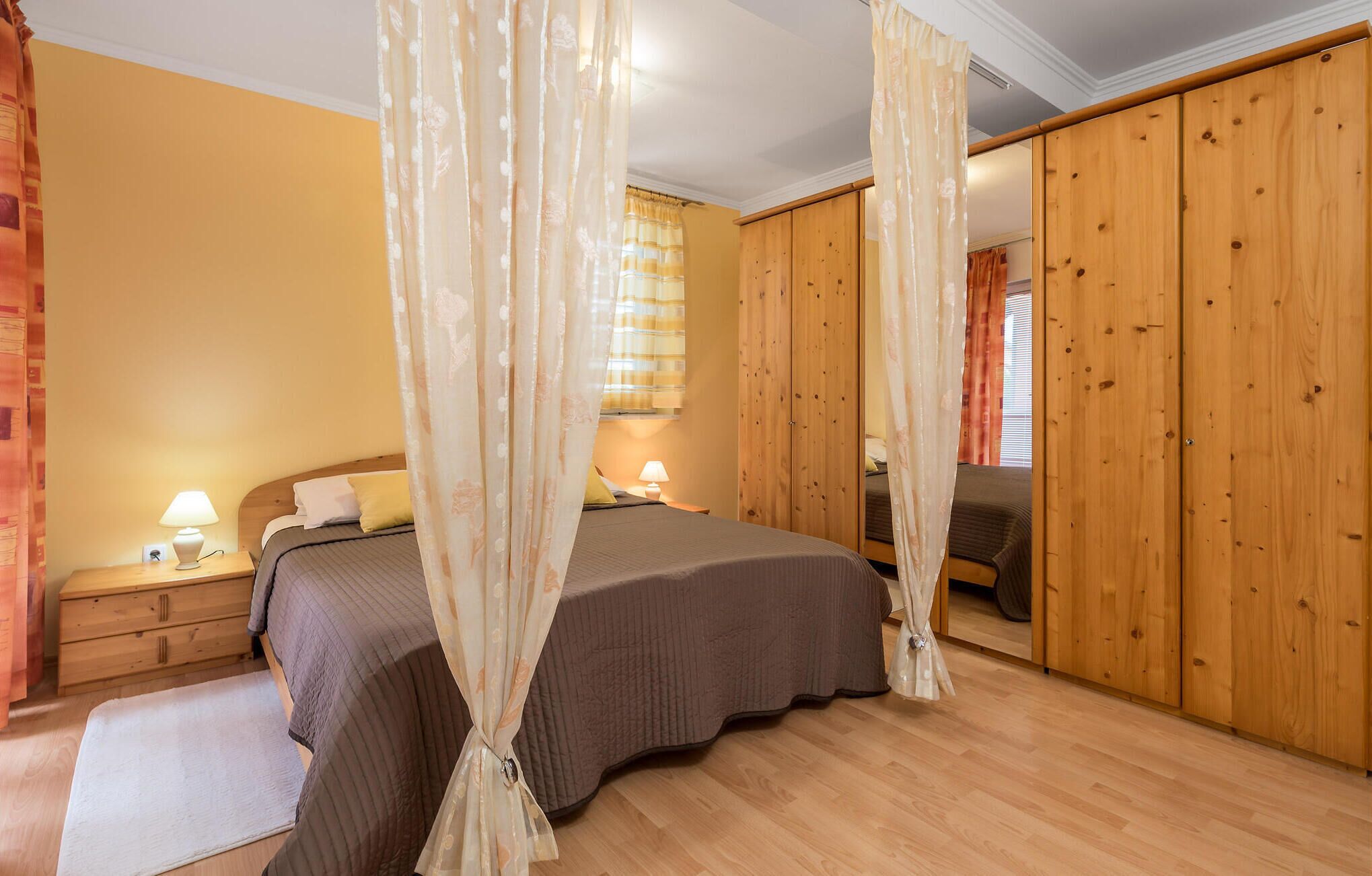 Een slaapkamer met een bed, een houten garderobe en een nachtkastje met een lamp.