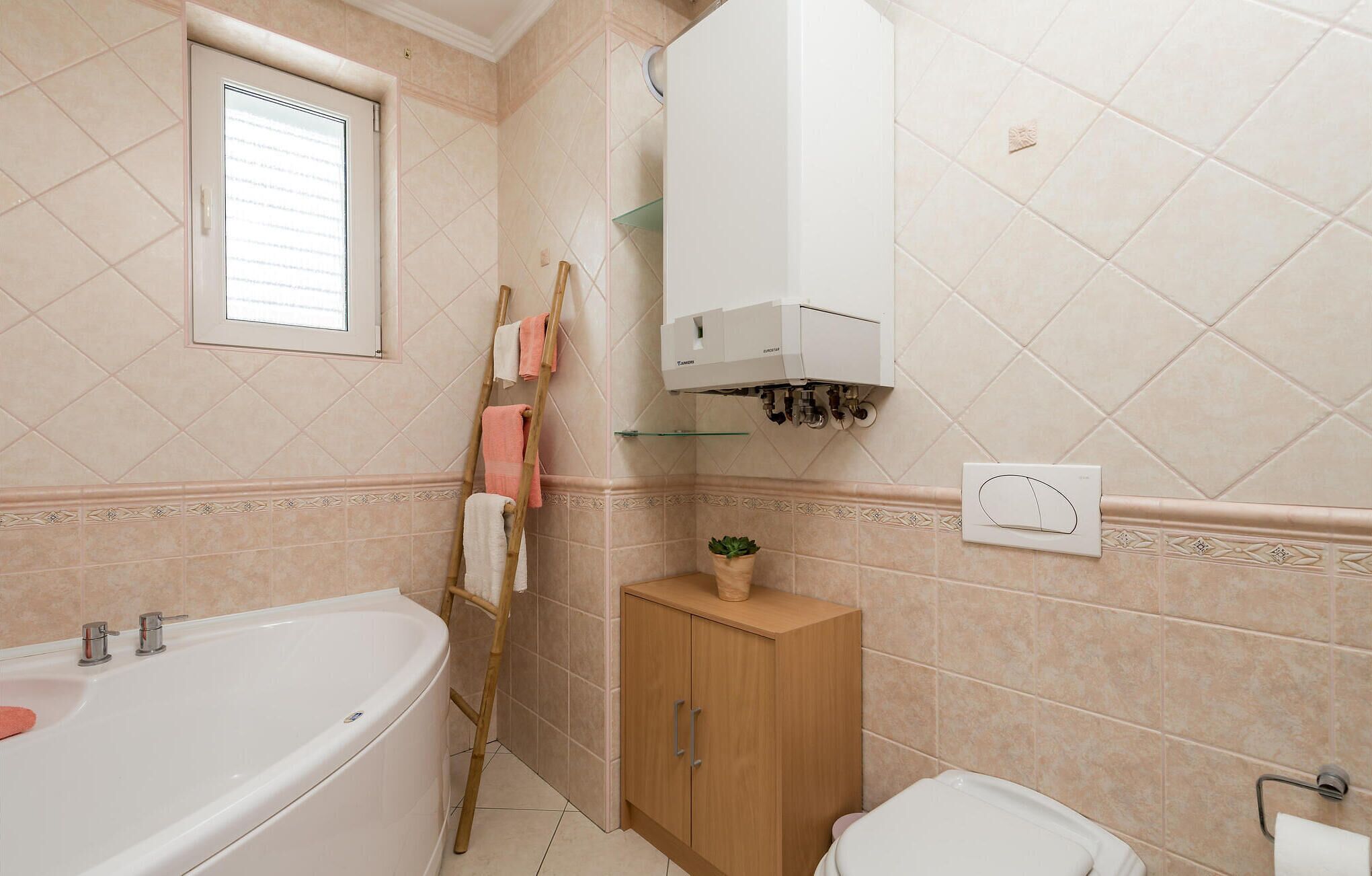 Une salle de bain avec une baignoire, un meuble en bois, un porte-serviettes et une fenêtre.