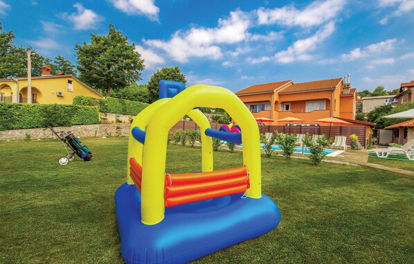 A backyard with a blue and yellow inflatable play structure, a swimming pool, and a lawn.