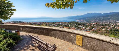 A stone bench overlooking a coastal town with a clear view of the sea and mountains in the distance.