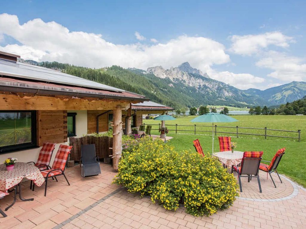 Eine Terrasse mit Sitzgelegenheiten im Freien, Blick auf Berge und ein Holzhaus.