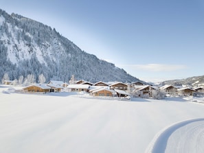 A snow-covered mountain village with wooden chalets, a clear sky, and a ski slope.
