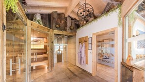 Eine geräumige Hotelhalle mit Holzboden, Glaswänden und einer hohen Decke mit freiliegenden Balken. Holzliegen und ein Kamin sind vorhanden.